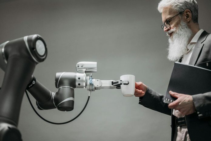 Photo by Pavel Danilyuk An elderly man receives a cup from a robotic arm in a modern office setting.